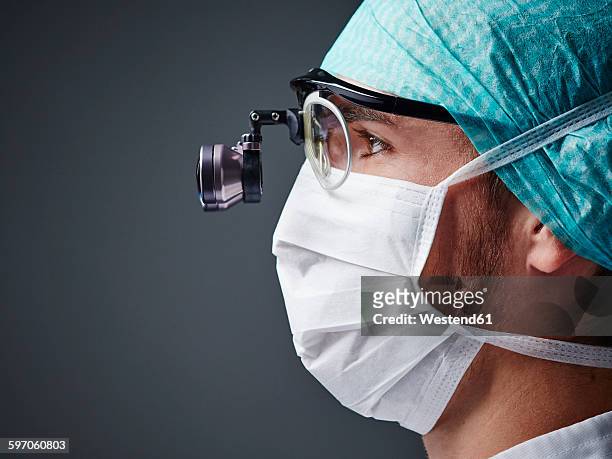 young doctor wearing mask and magnifying spectacles - doctor profile view stock pictures, royalty-free photos & images