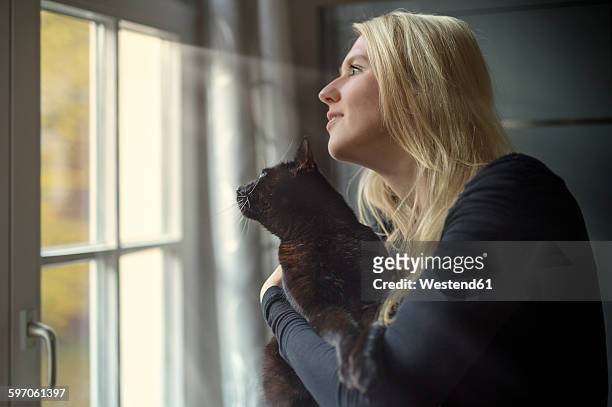 woman and her cat looking through the window at home - black and white cat foto e immagini stock