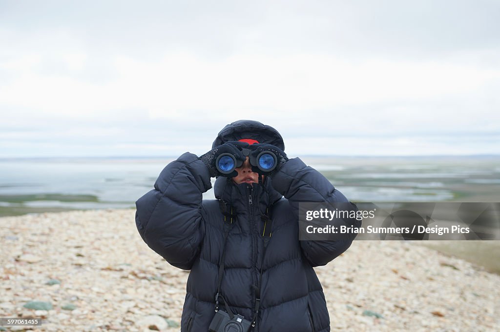 Teenager looking through binoculars on Mount Pelly, Ovayok Territorial Park, near Cambridge Bay