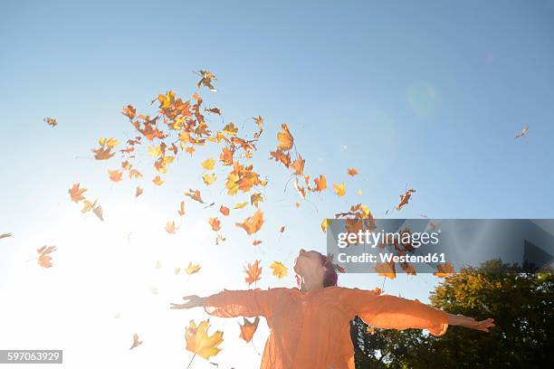 young woman throwing autum leaves in the air - euforie stockfoto's en -beelden