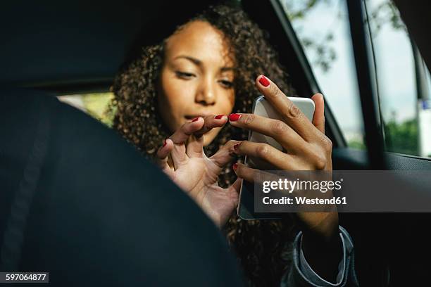 young woman sitting on back seat of a car using smartphone - esmalte de uñas rojo fotografías e imágenes de stock