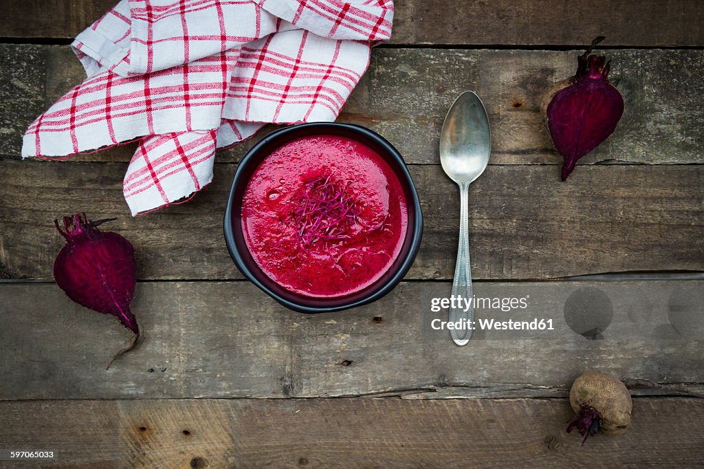 Bowl of beetroot soup garnished with beetroot sprouts on dark wood