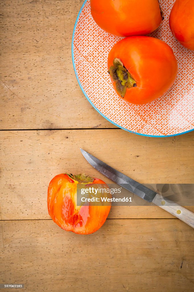 Whole and sliced kaki persimmons and a kitchen knife on wood