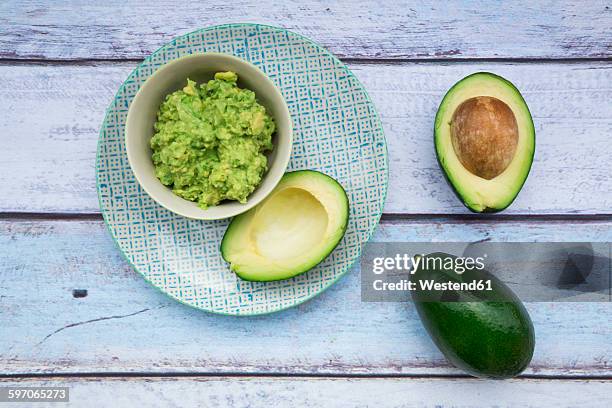 bowl of guacamole and whole and sliced avocados on light blue wood - guacamole stock-fotos und bilder