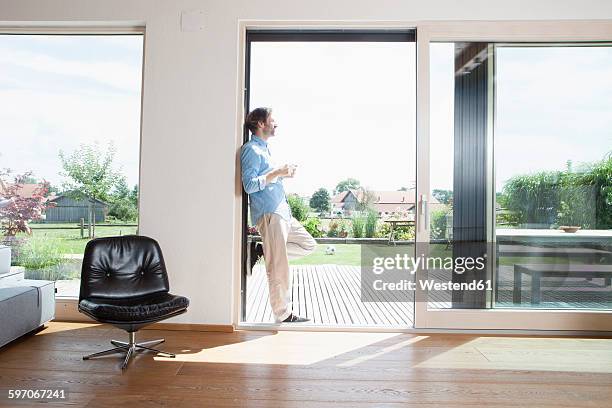 mature couple leaning in garden door with cup of coffee - man leaning chair standing side view stock pictures, royalty-free photos & images