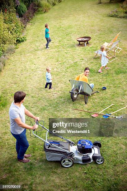 father mowing the lawn in garden with family playing in grass - lawnmowing stock pictures, royalty-free photos & images