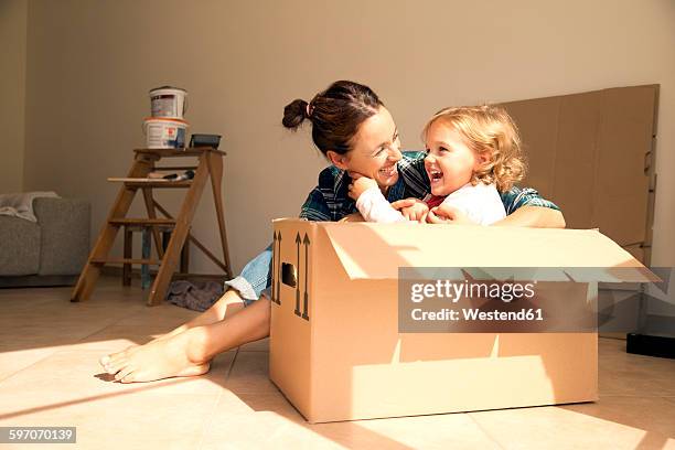 laughing woman with daughter sitting in cardboard box - new house imagens e fotografias de stock