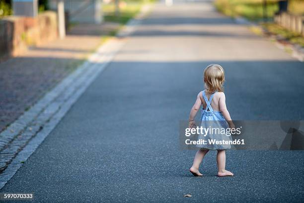 back view of barefoot blond little girl walking on empty road - blond hair girl fotografías e imágenes de stock