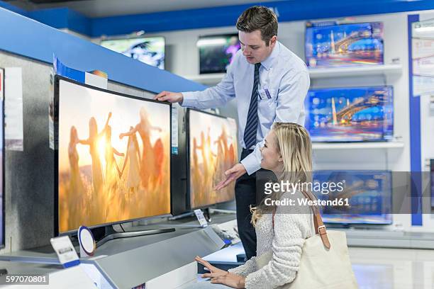shop assistant showing flatscreen tv to customer - electronic store fotografías e imágenes de stock