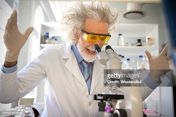 tousled professor examining samples under microscope, looking surprised - mad professor stock pictures, royalty-free photos & images