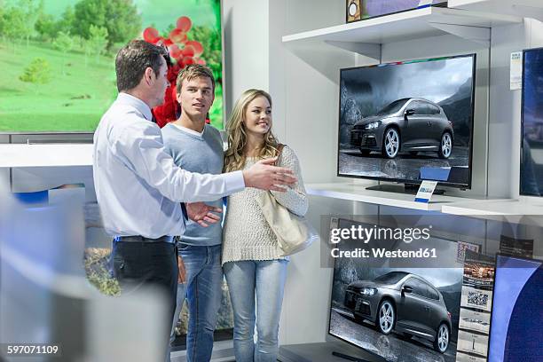 shop assistant showing flatscreen tvs to young couple - retailer shopping customer tv stockfoto's en -beelden