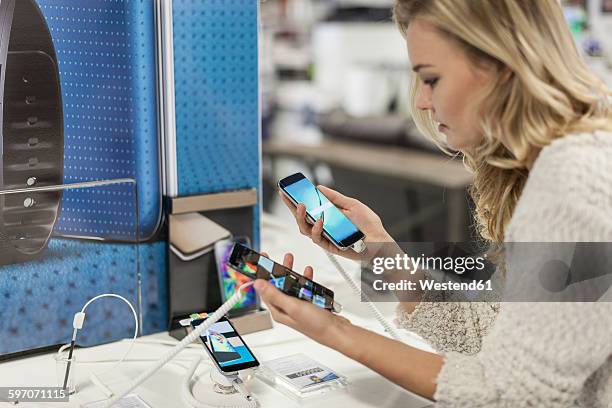 young woman comparing two smartphones in a shop - appliance store stockfoto's en -beelden