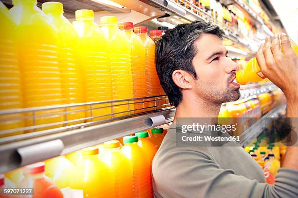 man drinking a bottle of orange juice in front of fridge in a supermarket - multiple same person stock pictures, royalty-free photos & images