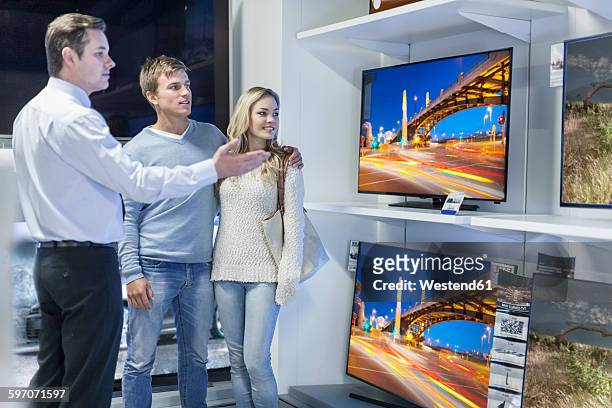 shop assistant showing flatscreen tvs to young couple - tv store stock pictures, royalty-free photos & images