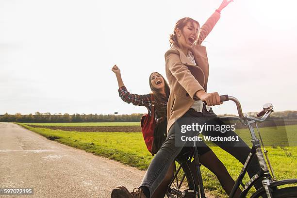 two exuberant young women sharing a bicycle in rural landscape - movendo um veículo - fotografias e filmes do acervo