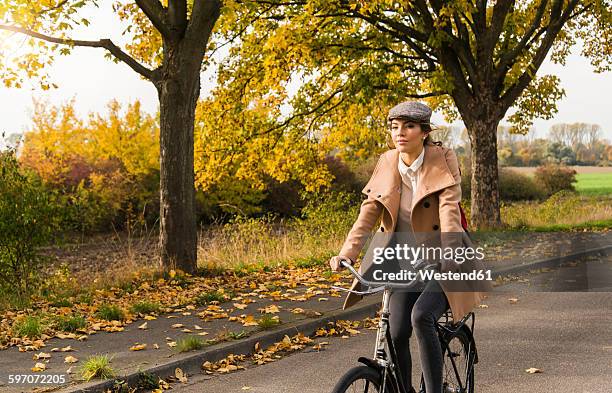 young woman riding bicycle in autumn landscape - velofahren stock-fotos und bilder