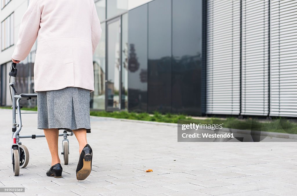 Senior woman walking with wheeled walker on pavement