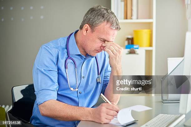 stressed gp sitting at desk - general practitioner stock pictures, royalty-free photos & images