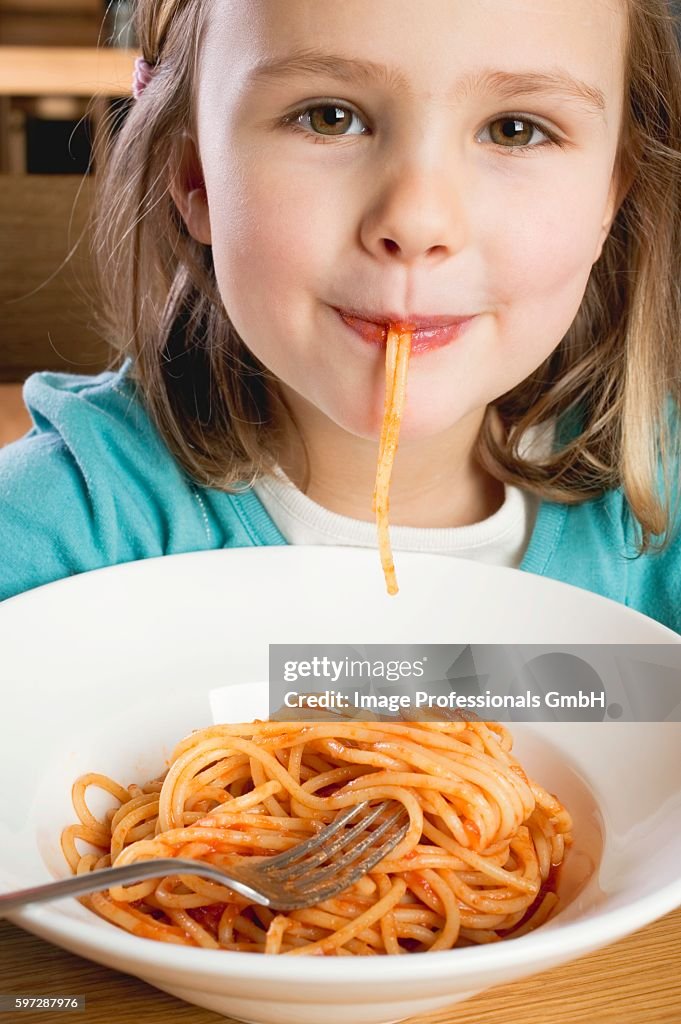Small girl eating spaghetti with tomato sauce