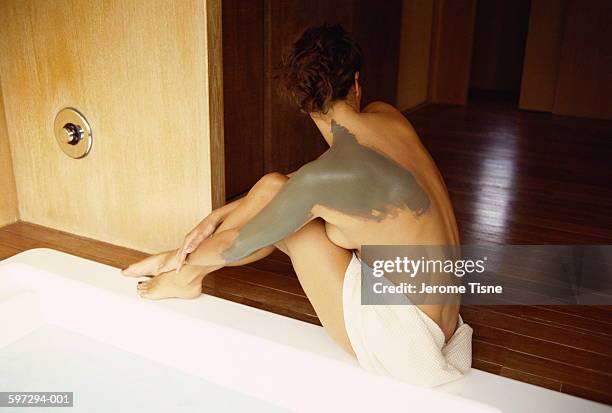 naked woman sitting on edge of pool, mud mask on arm and shoulder - mud foto e immagini stock