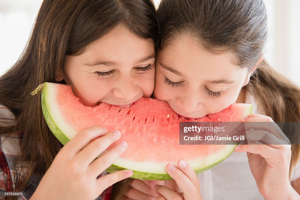 Caucasian twin sisters eating watermelon