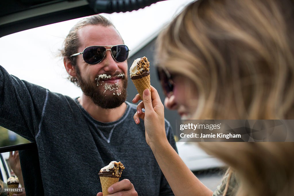 Young couple next to jeep messily eating ice cream cones