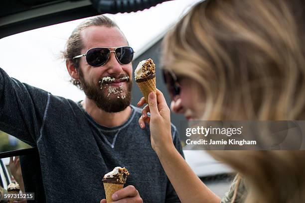 young couple next to jeep messily eating ice cream cones - gedeelde mobiliteit stockfoto's en -beelden