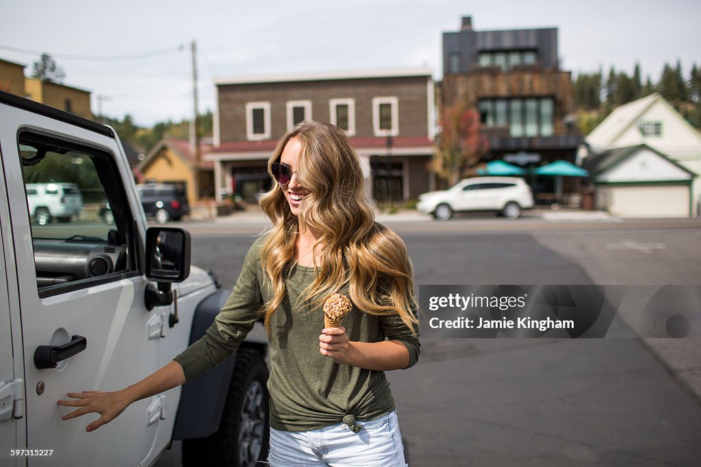 Young woman with long blond hair holding ice cream next to jeep