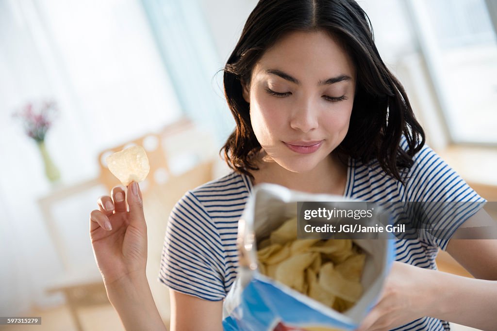 Hispanic woman reading ingredients on bag of potato chips