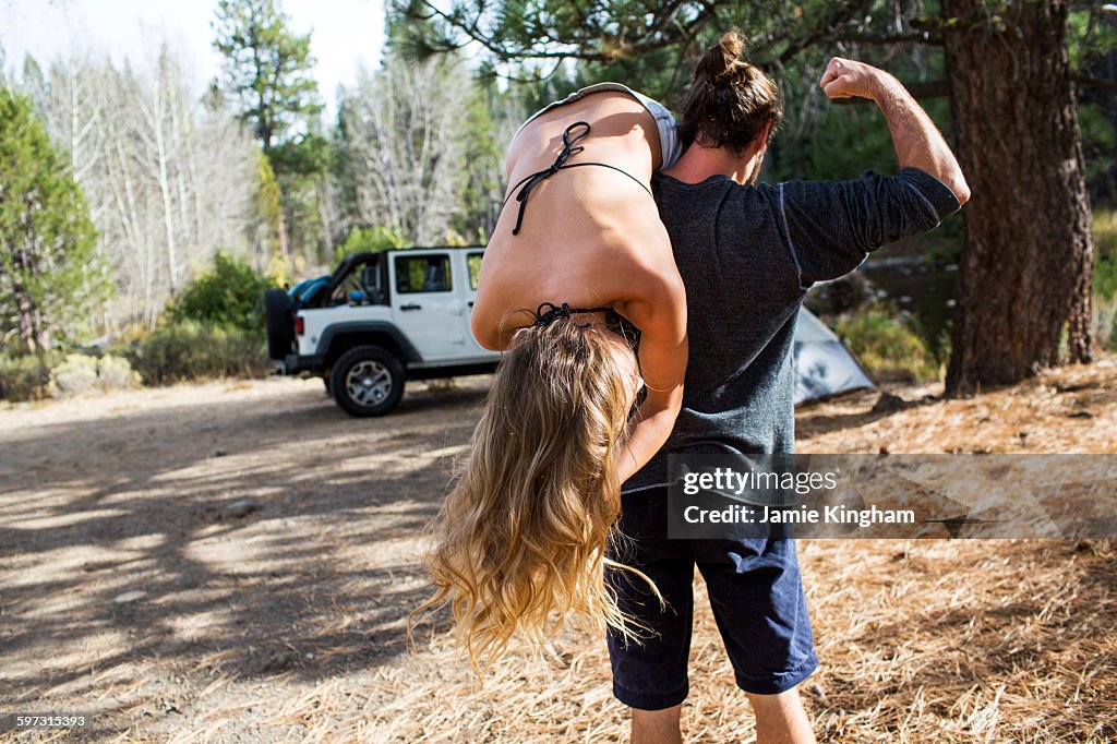 Rear view of young man carrying girlfriend over shoulder at forest campsite, Lake Tahoe, Nevada, USA