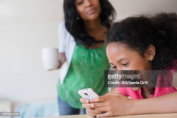 mother watching daughter use cell phone - private viewing stock-fotos und bilder