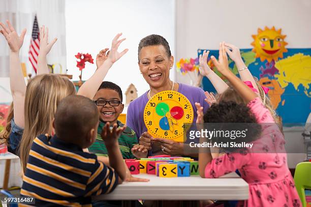kindergarten students and teacher reading clock - clock person desk stockfoto's en -beelden