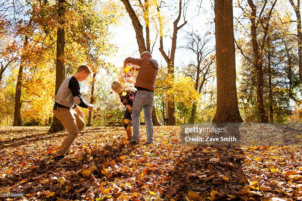 Young woman playfighting with two teenage brothers in autumn forest