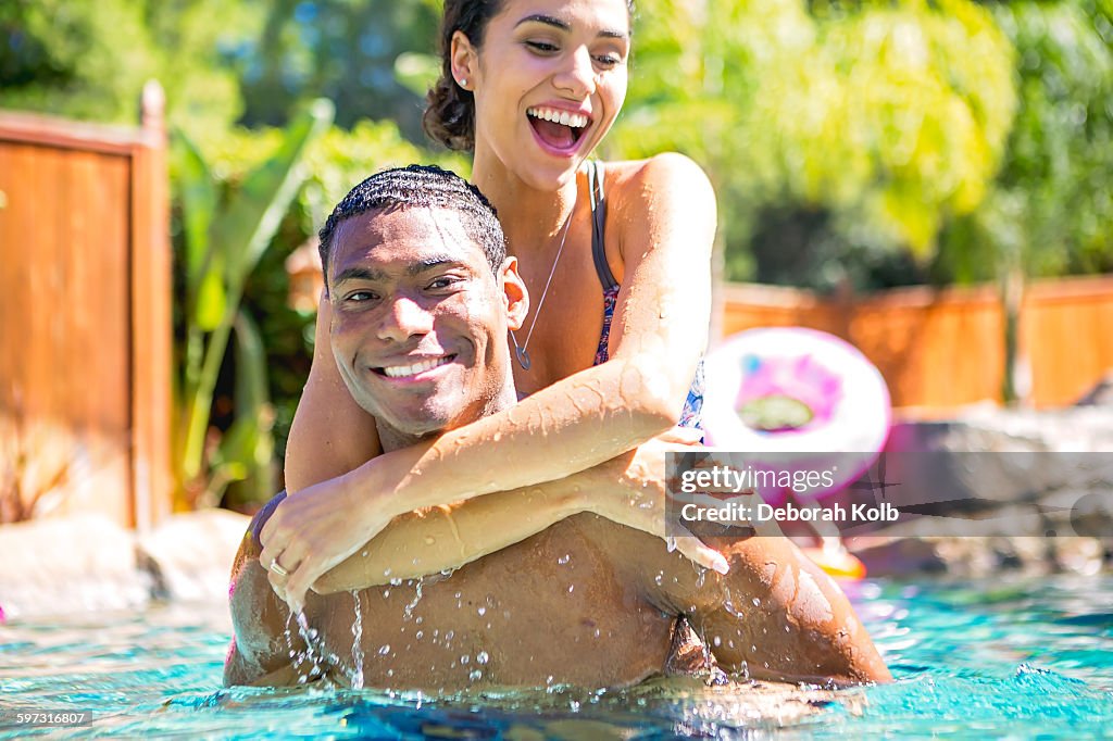 Mid adult man carrying young woman on back in swimming pool looking at camera smiling