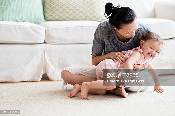 mother and baby daughter playing in living room - tickling stock-fotos und bilder