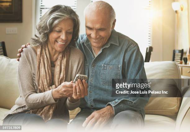hispanic couple using cell phone on sofa - wife stock pictures, royalty-free photos & images