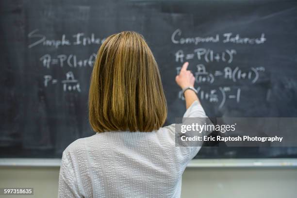 caucasian teacher pointing to chalkboard - maestra foto e immagini stock