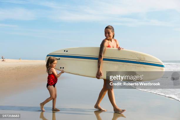 mother and daughter carrying surfboard on beach - beach hold surfboard stock-fotos und bilder