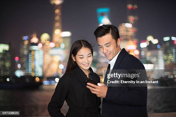 young couple looking at phone in the city at night - östasiatiskt ursprung bildbanksfoton och bilder