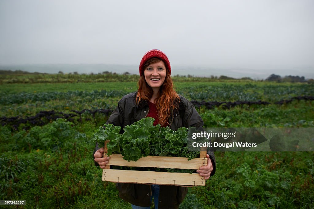 Portrait of woman holding box of kale on farm.