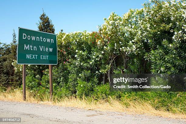 Road sign along California Highway 237 for the Silicon Valley town of Mountain View, California, with red and white flowers in the background,...