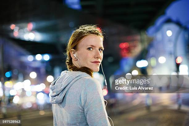 female runner listening music on city street - woman looking over shoulder stock-fotos und bilder