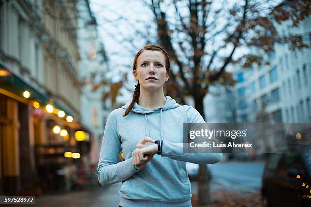 woman using watch before exercising on sidewalk - exactitud fotografías e imágenes de stock