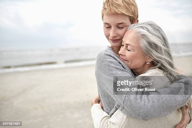 adult daughter hugging senior mother on the beach - nur erwachsene stock-fotos und bilder