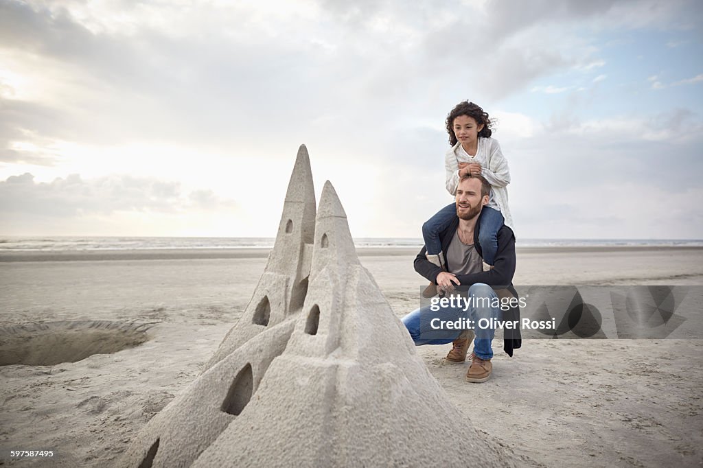 Father and daughter on beach looking at sandcastle