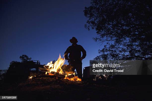 man with hat standing by campfire. - australia fire - fotografias e filmes do acervo