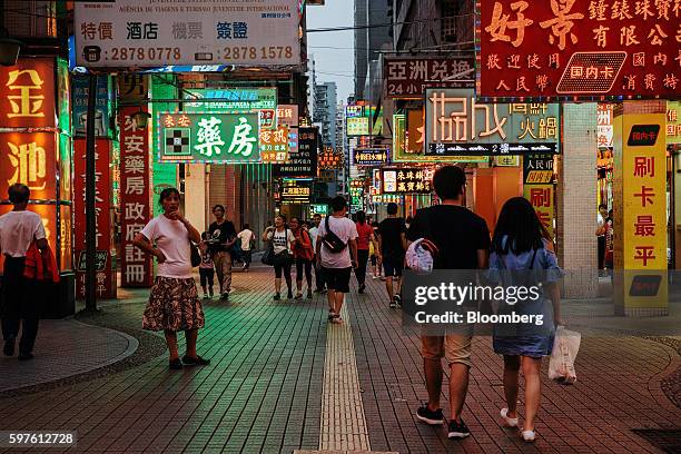 Pedestrians walk along a street with illuminated signs at night in Macau, China, on Sunday, Aug. 28, 2016. Macau is scheduled to release gross...