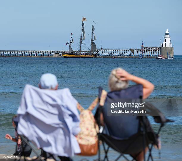 Couple sit on the beach and watch as the Russian ship Shtandart leaves Blyth harbour during the North Sea Tall Ships Parade of Sail on August 29,...