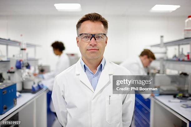 scientist in laboratory, colleagues working in background - scientist standing stock-fotos und bilder