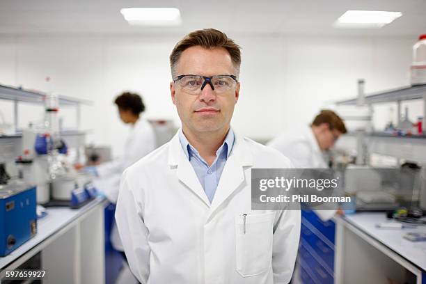 scientist in laboratory, colleagues working in background - scientist clean suit stock pictures, royalty-free photos & images